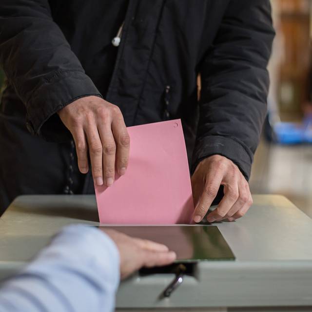 Ein Stimmzettel in einem Umschlag wird in eine Wahlurne eingeworfen.