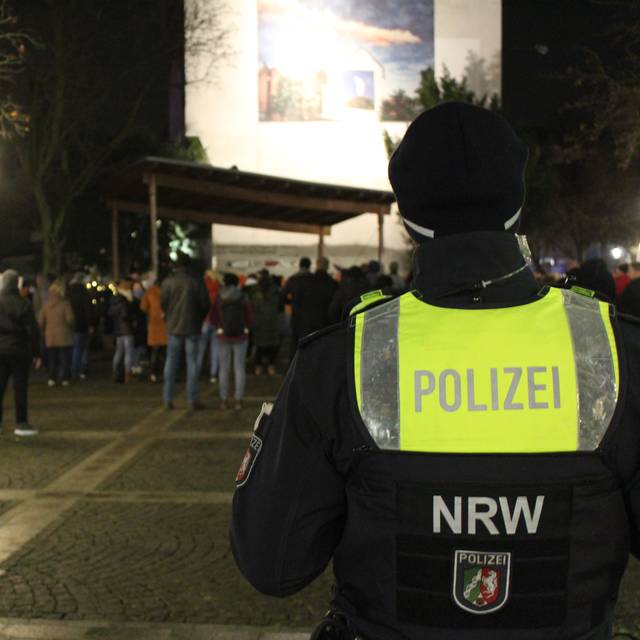 Ein Polizist steht mit dem Rücken zur Kamera vor einer Gruppe Demonstranten.