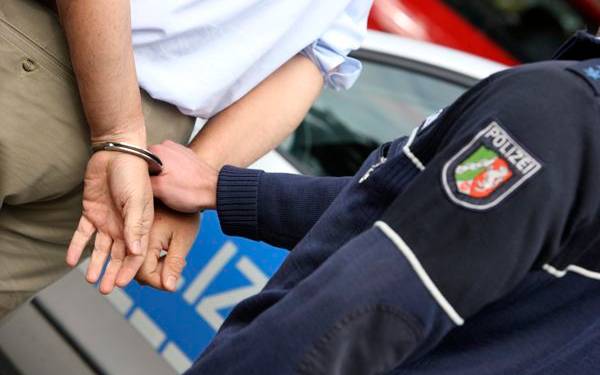 Zu sehen ist eine Person von hinten, die gerade von einem Polizisten mit Handschellen festgenommen wird.