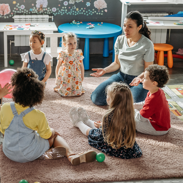 Eine Kita-Gruppe sitzt in der morgendlichen Besprechung mit Erzieherinnen.