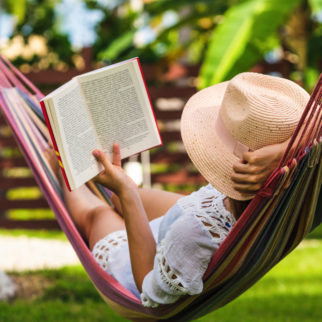 Eine Frau liest ein Buch in einer Hängematte im Garten.