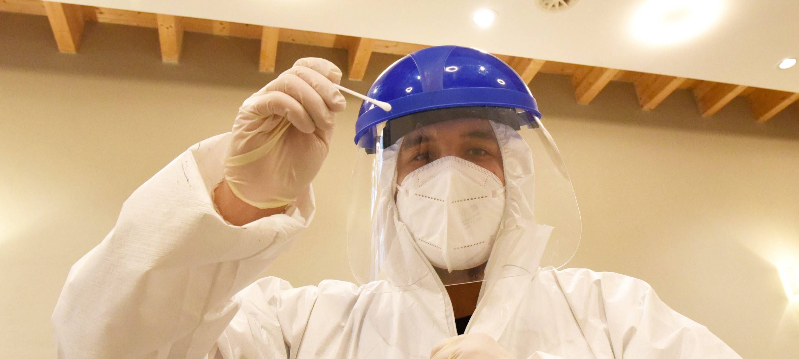 Mann in Schutzkleidung mit Teststäbchen in der Hand