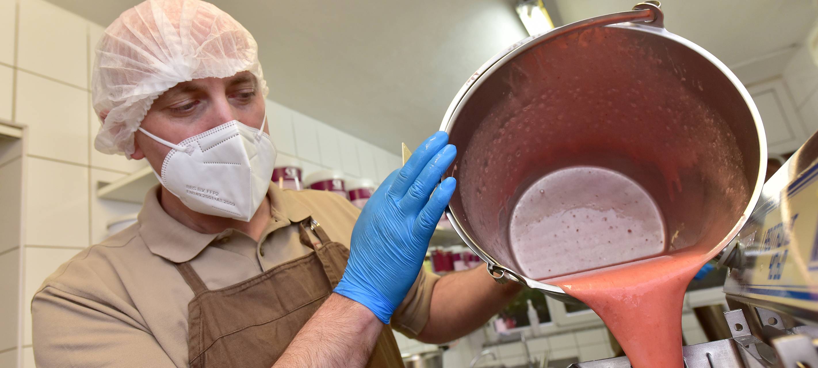 Der Chef der Eis Oase schüttet einen Topf mit pürierten Erdbeeren in eine größere Schüssel.
