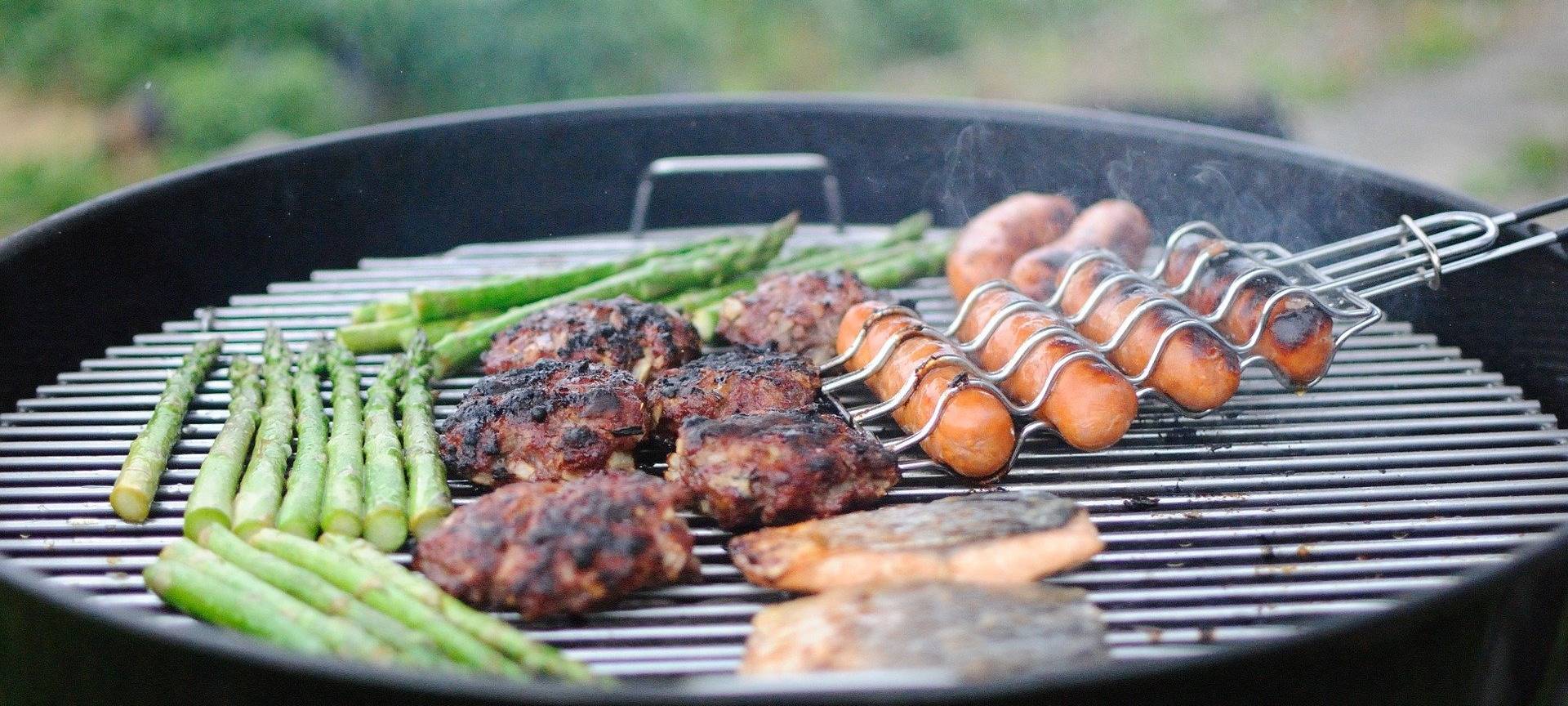 Würstchen, Fleisch und grüner Spargel werden auf einem Grill gegrillt.