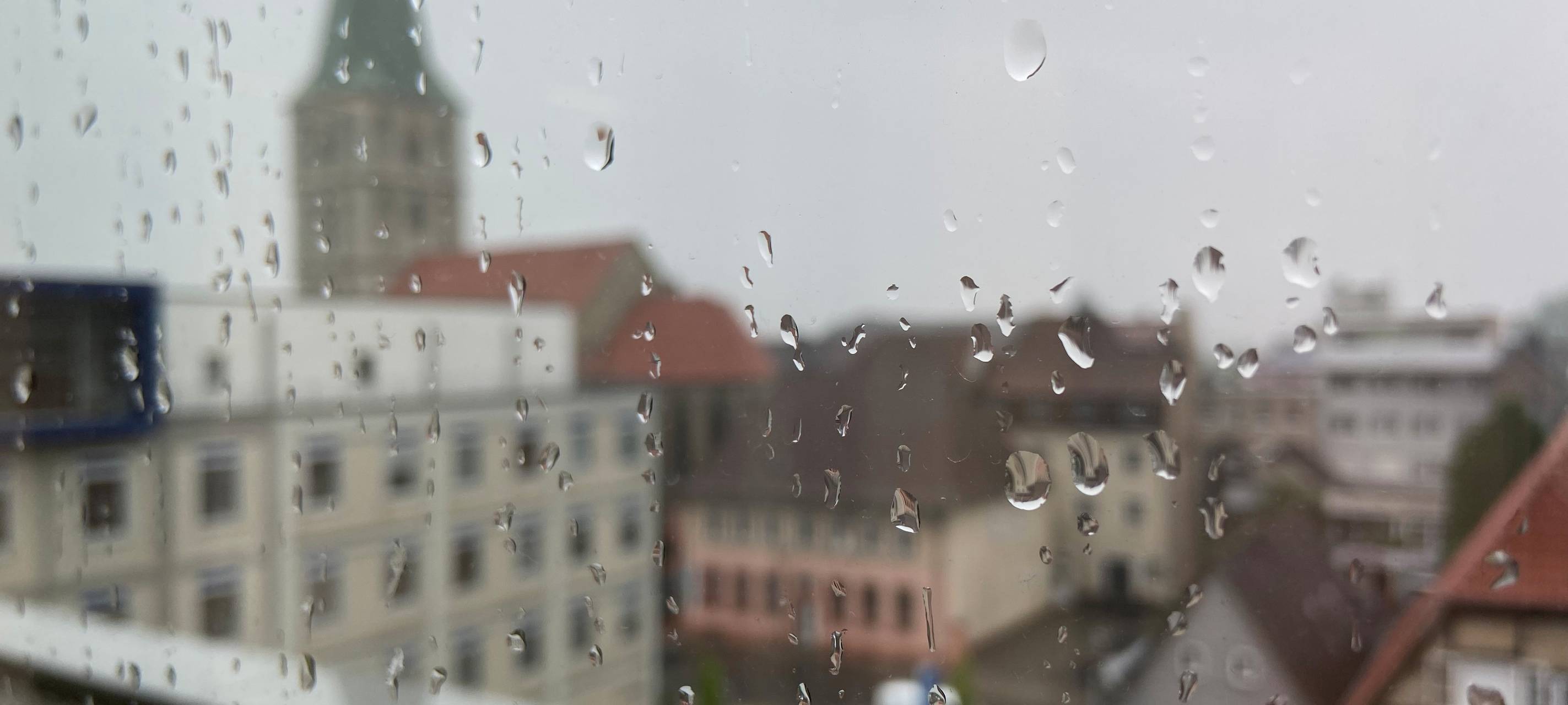Viele Wassertropfen hängen an einer Fensterscheibe. Im Hintergrund ist die Pauluskirche.