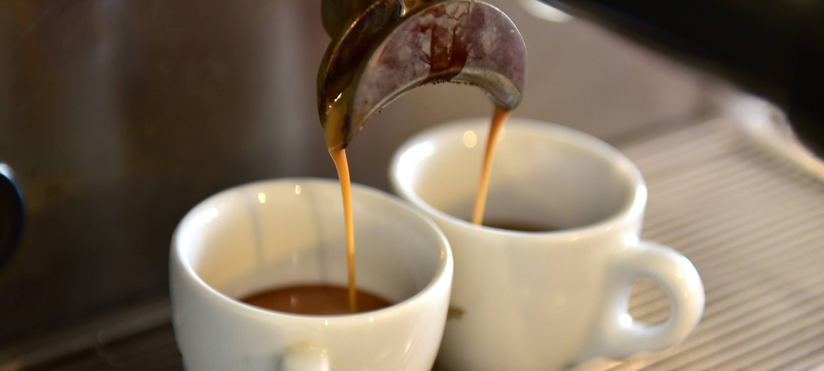 Zwei Tassen stehen unter einer Kaffeemaschine, aus der gerade frischer Kaffee läuft.