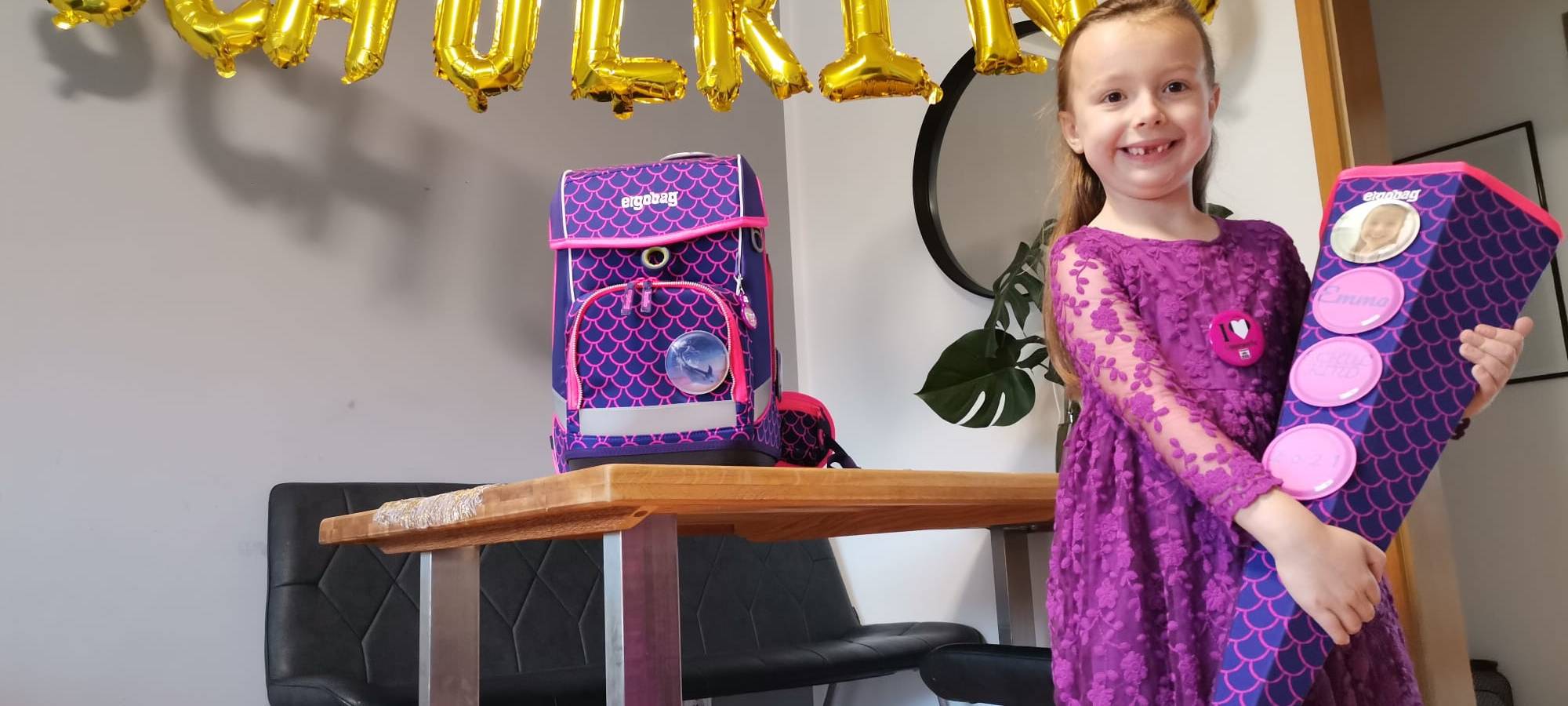Emma hat ein ein lila Kleid an und eine Lila Schultüte in der Hand.