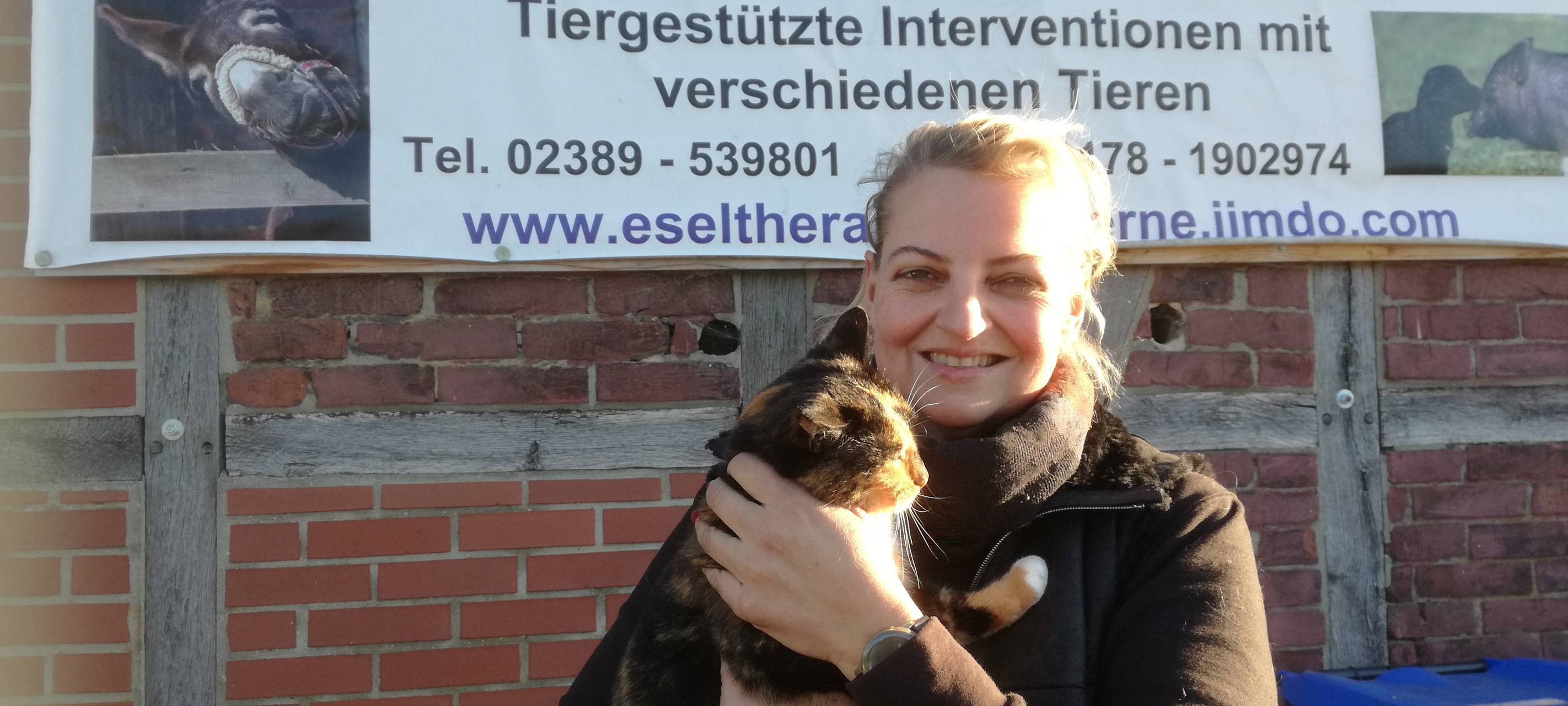 Bianca Terhüne steht mit einer Katze im Arm vor einem Banner.