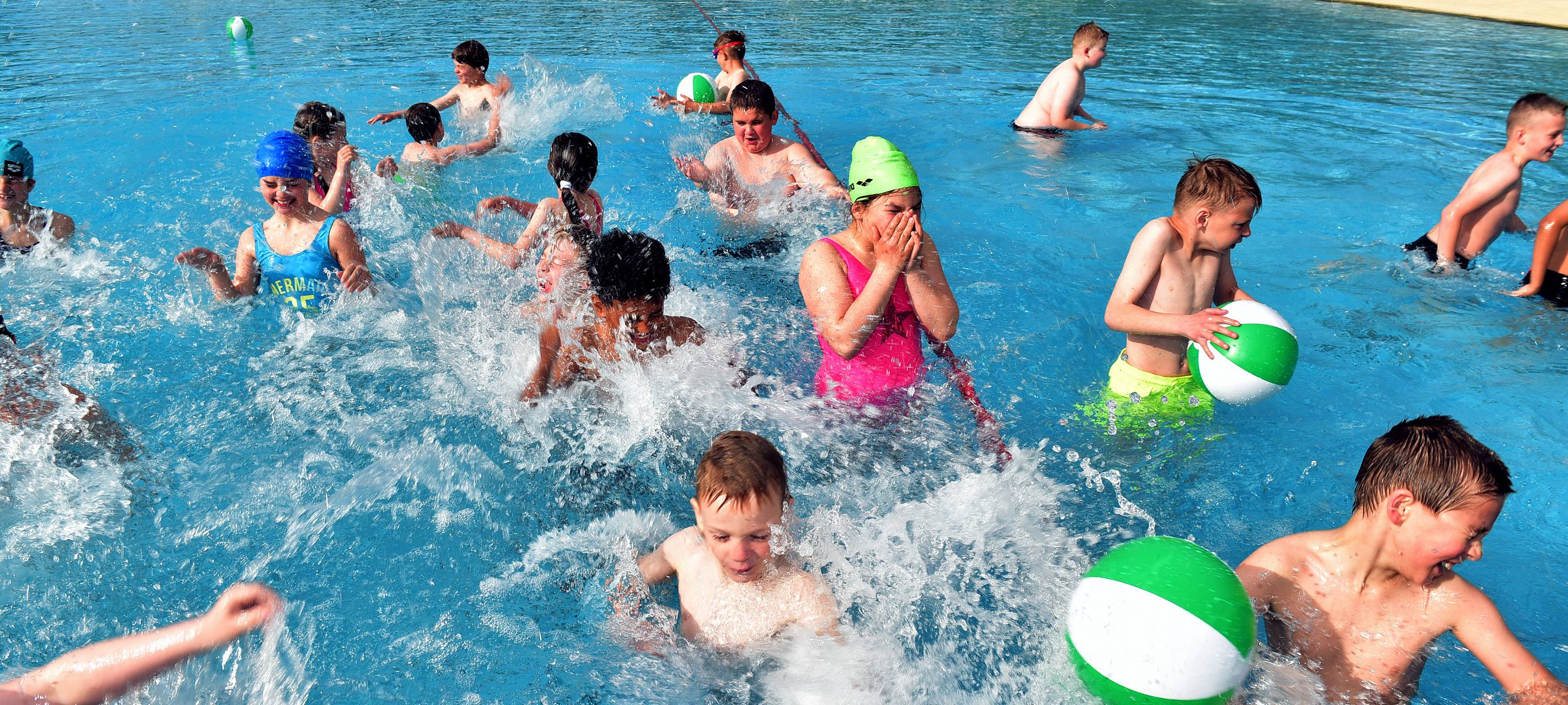 Viele Kinder sind im Wasser mit grünen Wasserbällen. Sie haben Spaß.
