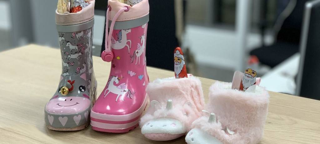 Vier kleine rosa Kinderstiefel, gefüllt mit Schokolaude auf einem Tisch.
