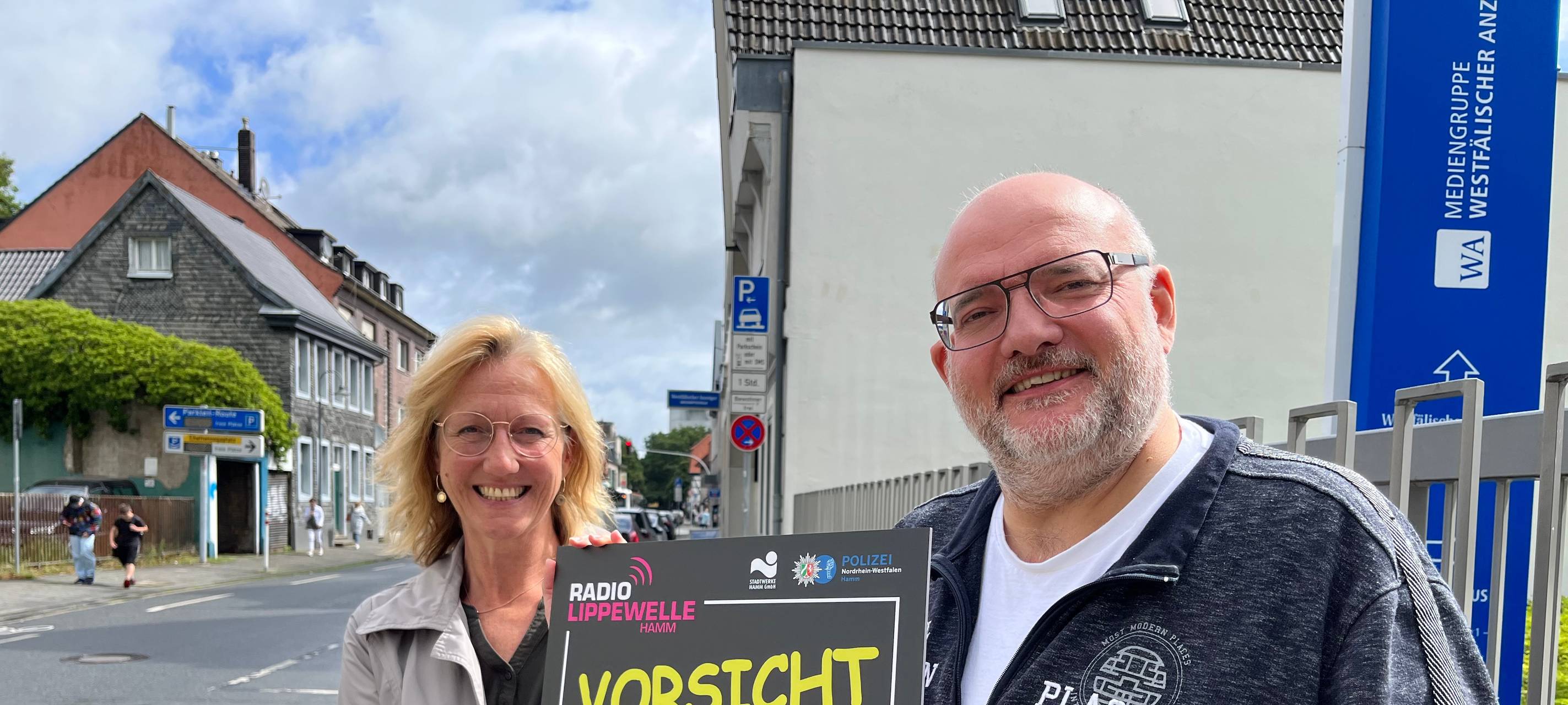 Simone Niewerth und Jens Heusener aus der Lippewelle-Morningshow zeigen das neue Schulstart-Schild