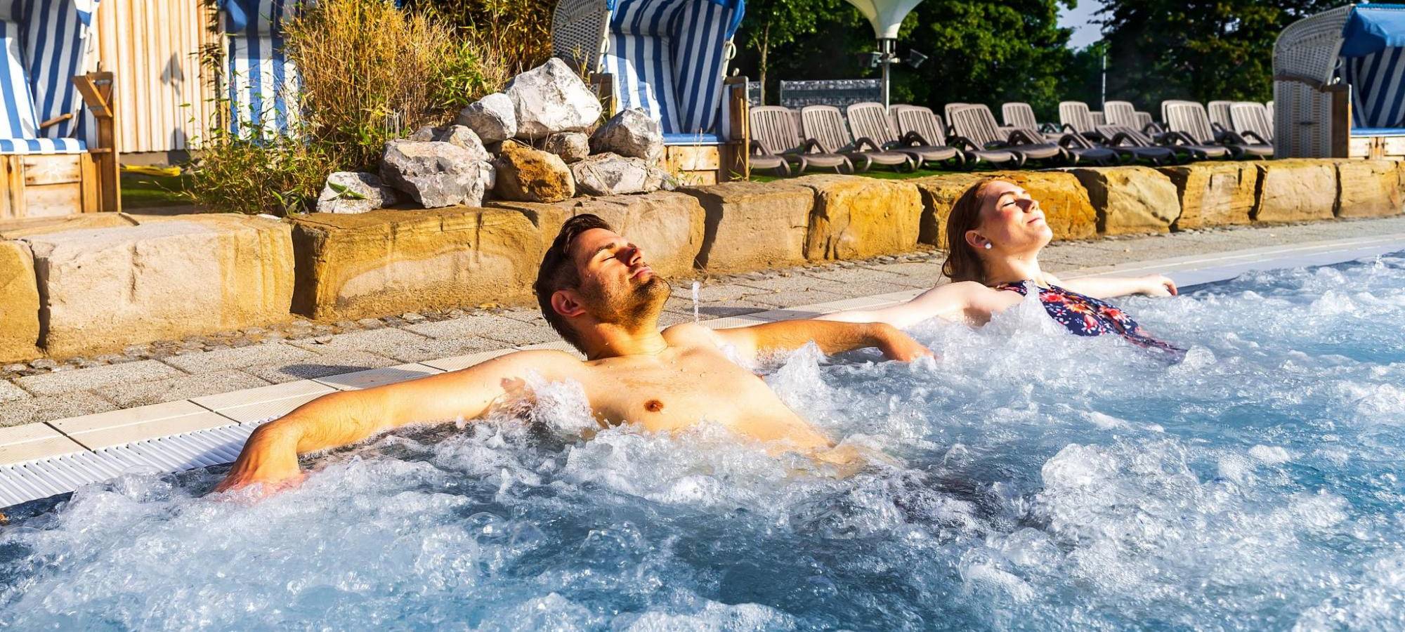Mann und Frau entspannen auf einer Sprudelliege im Außenbecken des Maximare