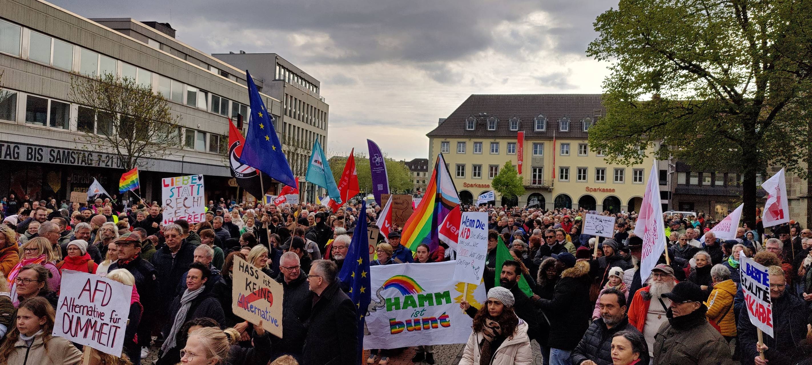 Viele Menschen stehen mit Bannern, bunten Fahnen und Plakaten auf dem Marktplatz vor der Pauluskirche.
