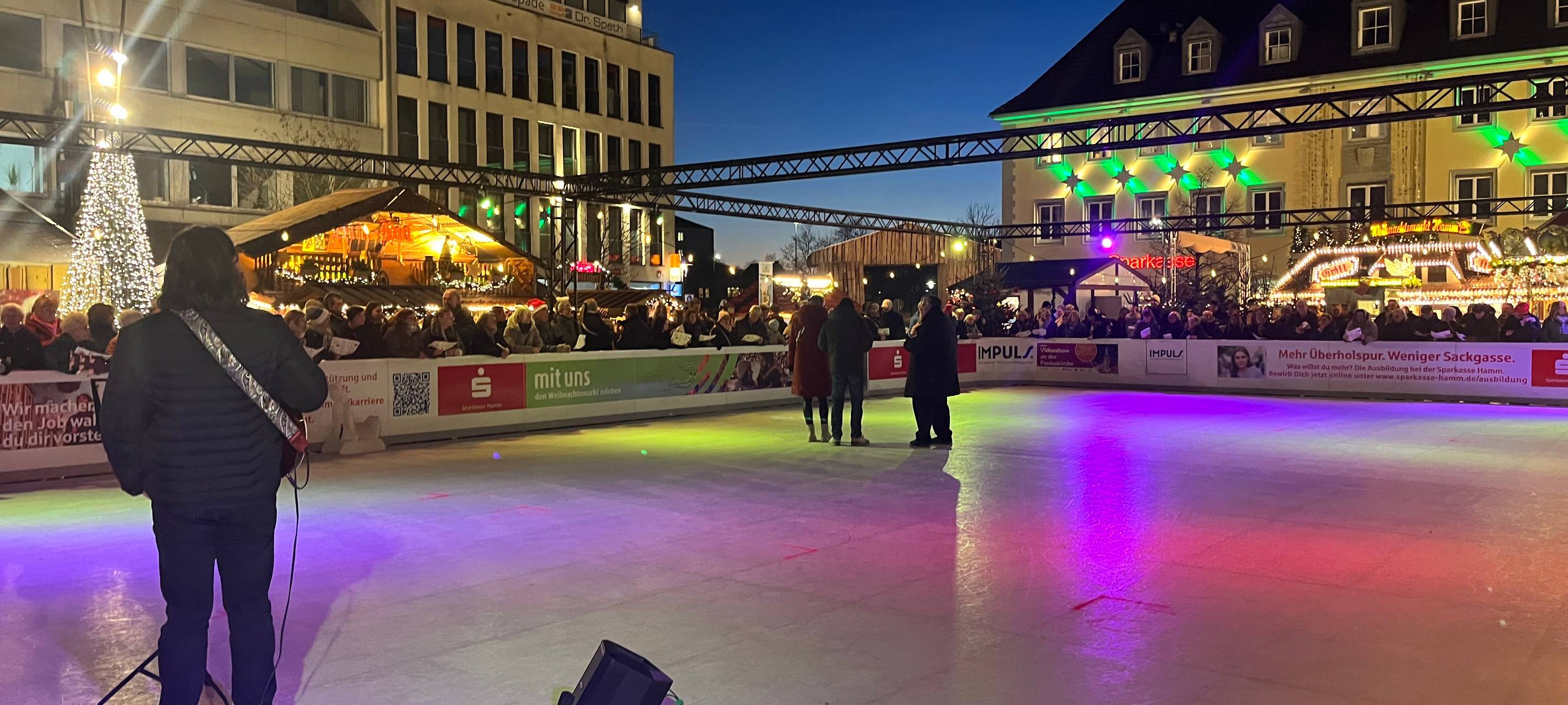 Die Eisfläche auf dem Hammer Weihanchtsmarkt mit singenden Menschen drum herum.