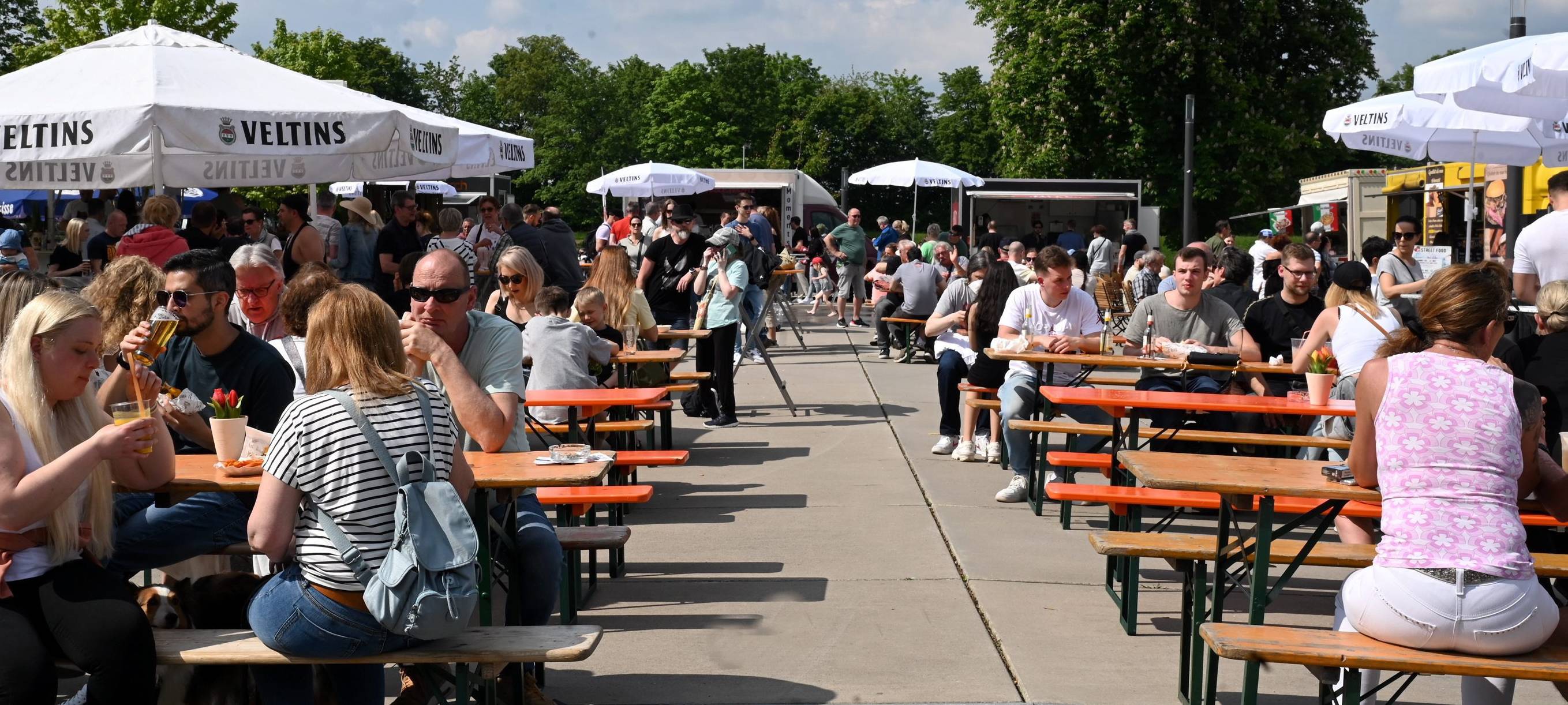 Menschen sitzen draußen auf Bierbänken und essen und trinken.