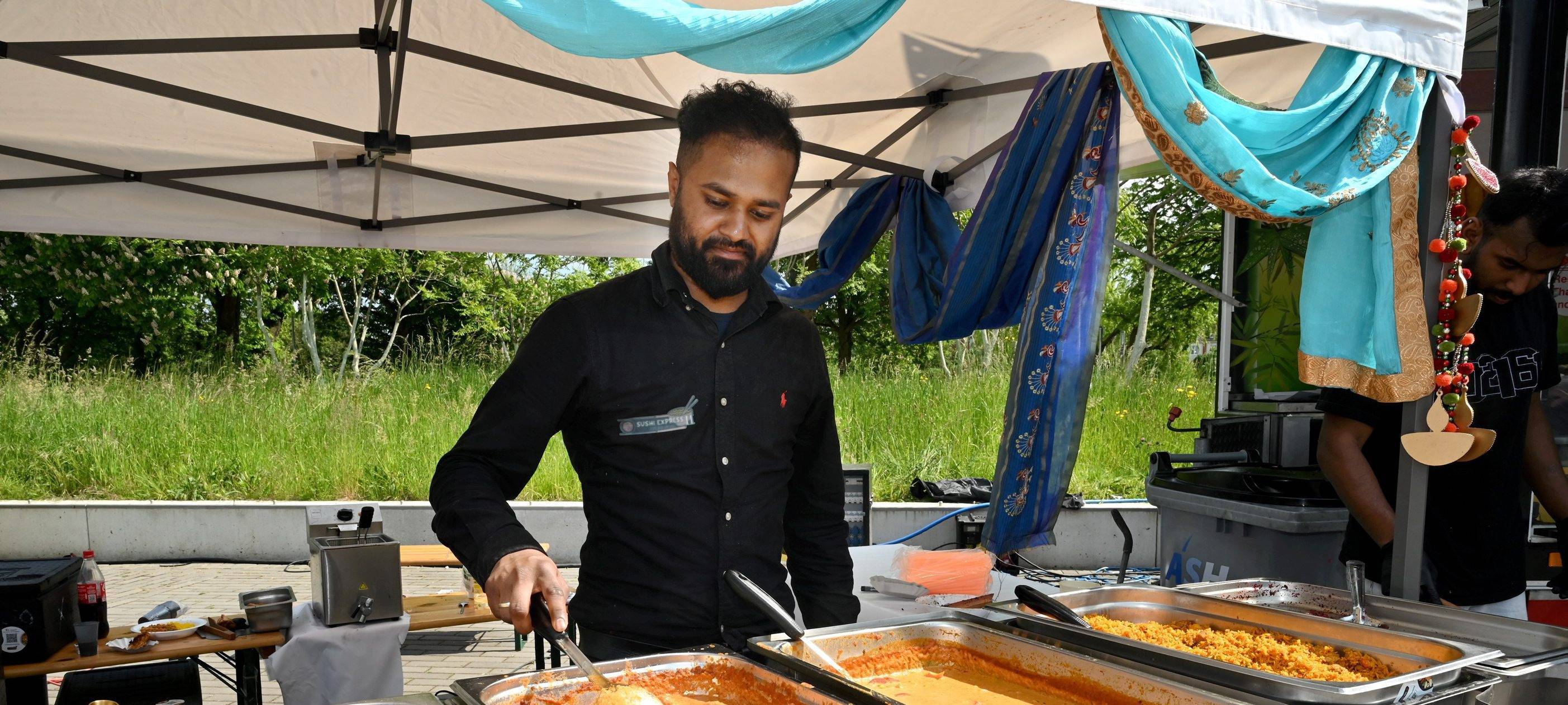 Ein Mann steht vor Warmhaltebehältern mit Curry.