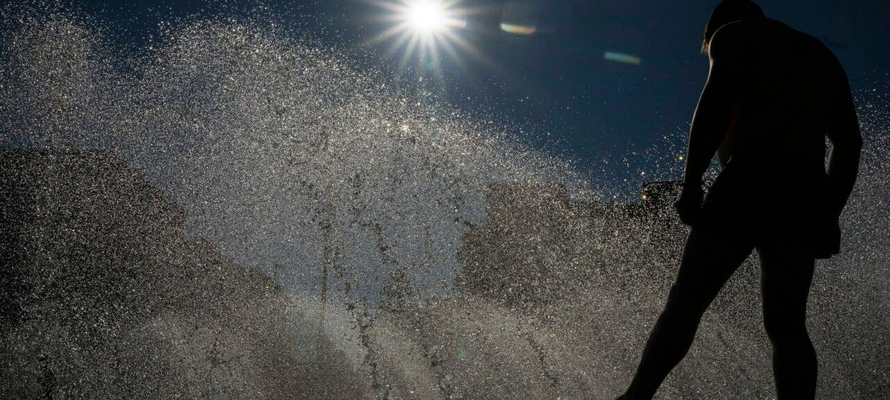 Ein Mann kühlt sich an einem Brunnen am Stachus in der Innenstadt im Wasser ab.