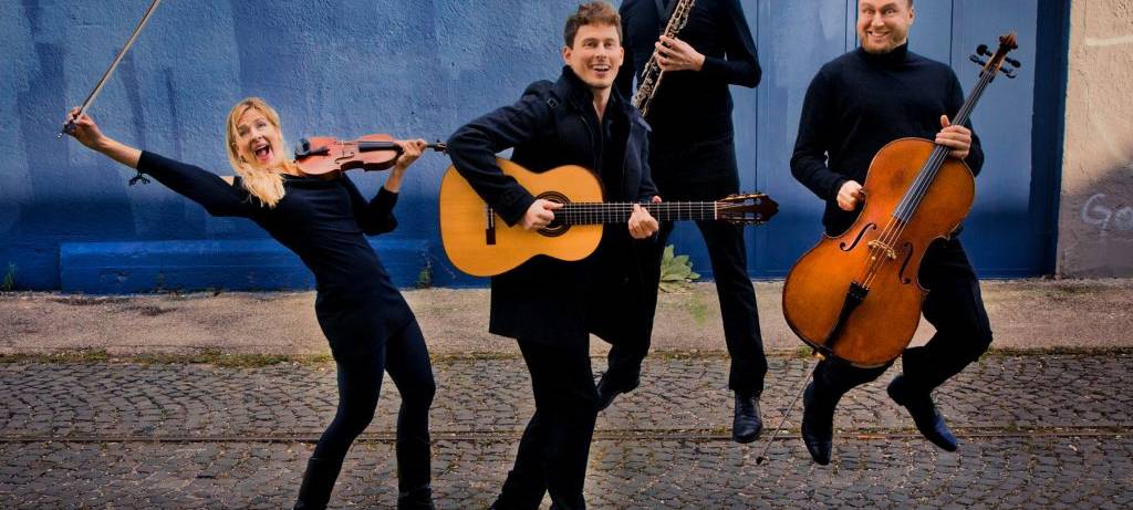 Vier Musiker springen vor einem blauen Hintergrund mit ihren Instrumenten in die Luft.