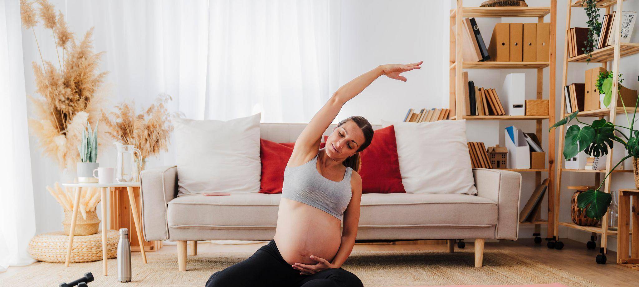 Eine Schwangere macht Dehnübungen auf einer Yogamatte