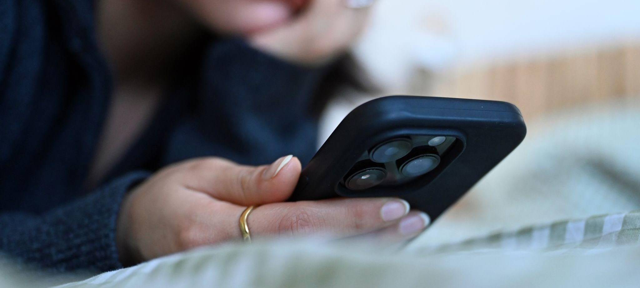 Frau liegt auf einem Bett und schaut auf ihr Smartphone