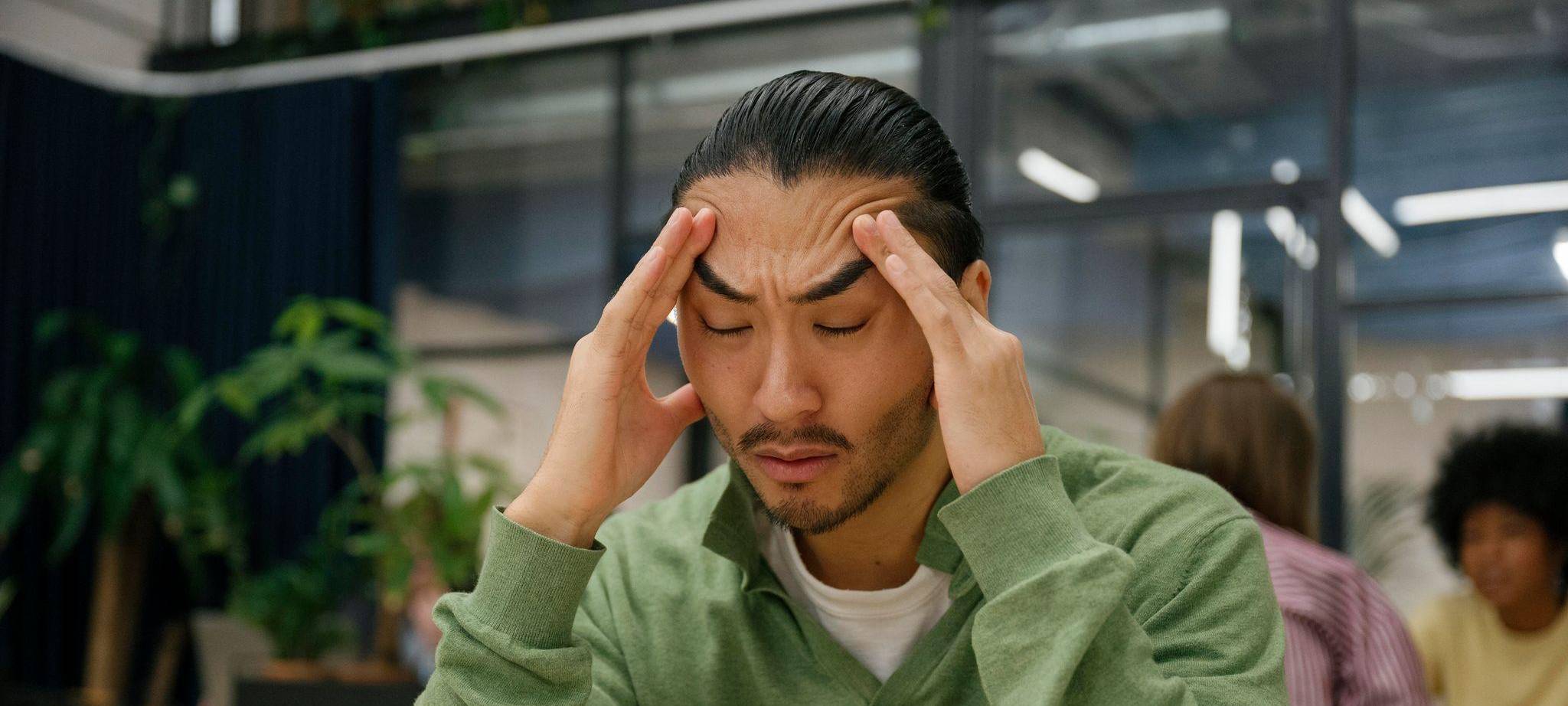 Ein Mann fasst sich an die Schläfen in einem Großraumbüro
