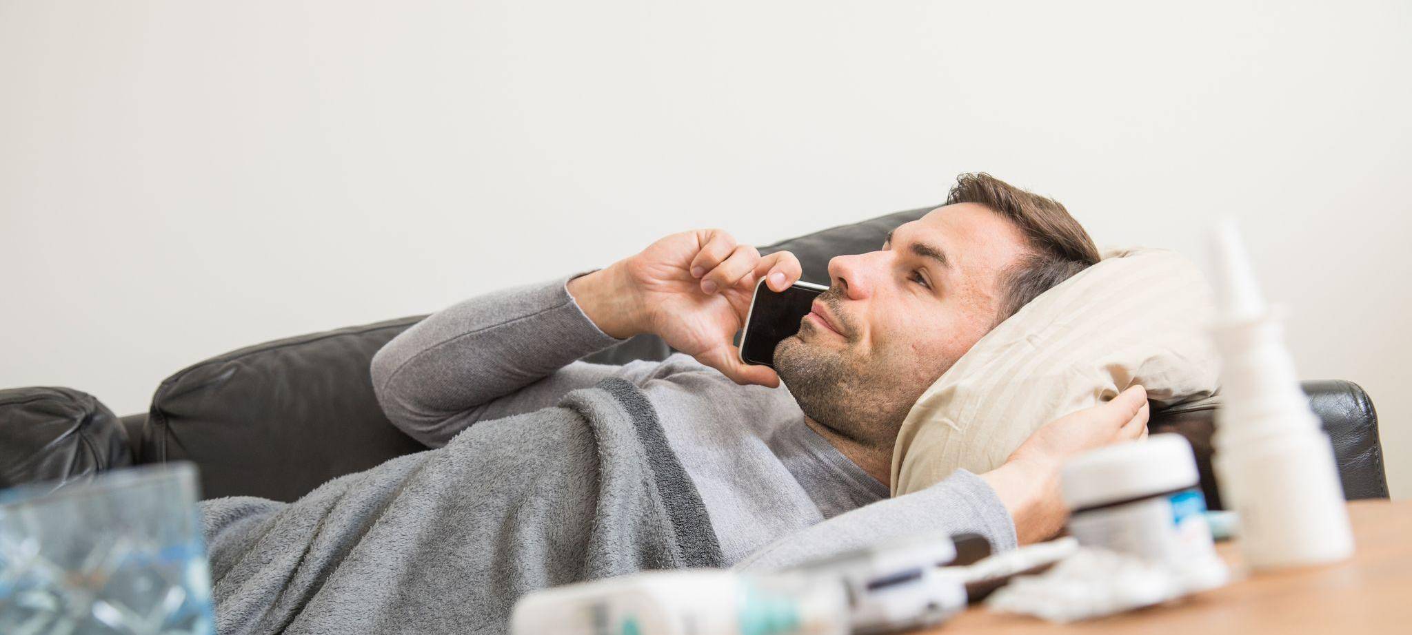 Ein Mann liegt krank auf einem Sofa und telefoniert