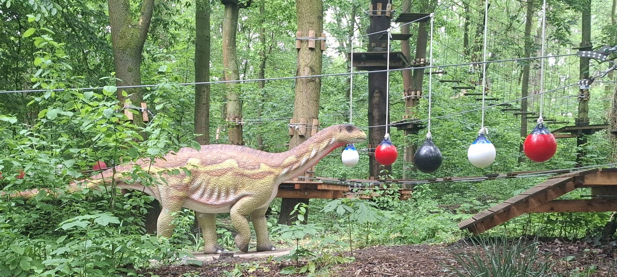 Ein künstlicher Dino steht neben einem Kletterparcours im Wald.