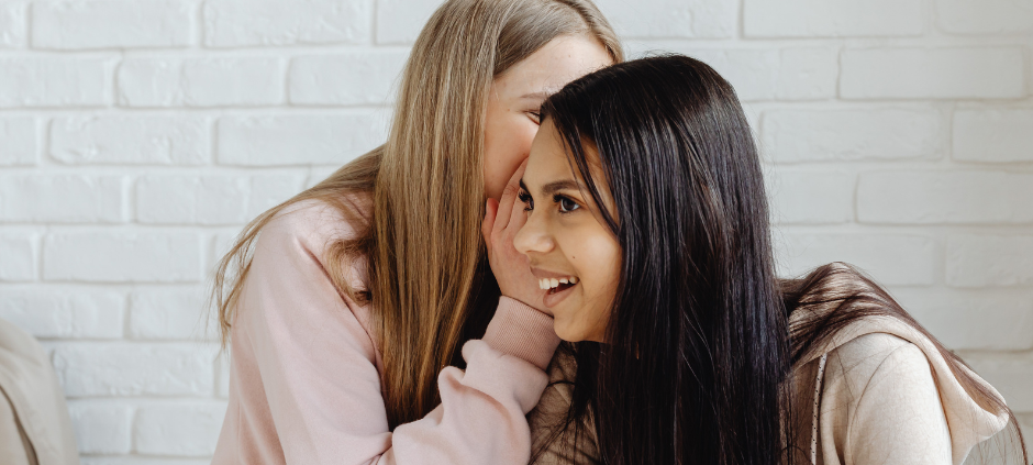 Eine Frau flüstert einer anderen etwas ins Ohr.