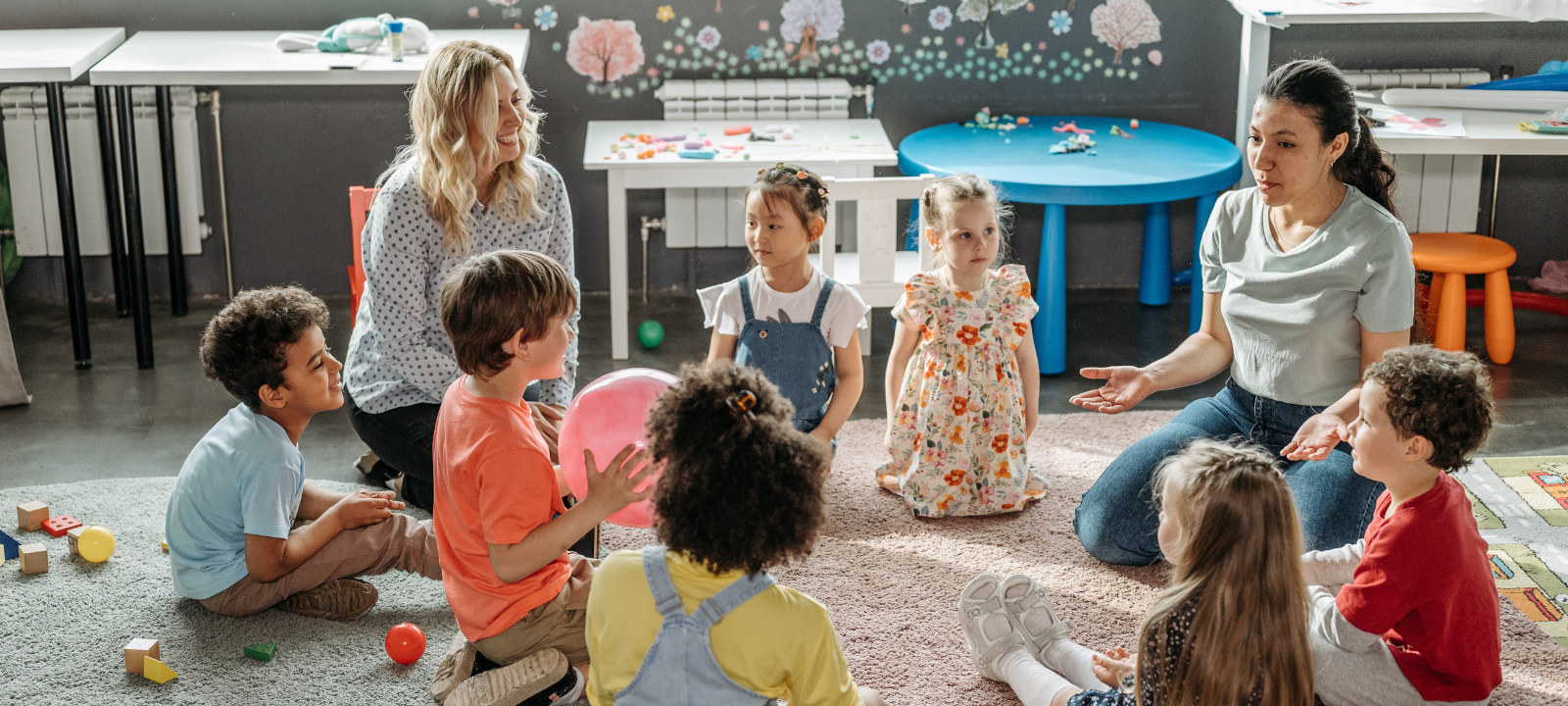 Eine Kita-Gruppe sitzt in der morgendlichen Besprechung mit Erzieherinnen.